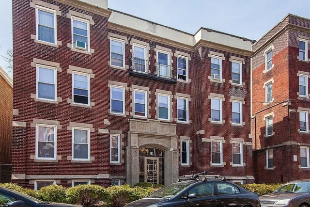 a front view of a building with lot of cars and trees