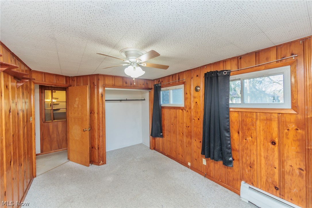38565 Sugar Ridge Road North Ridgeville, OH 44039 - Photo 34 of 49 Unfurnished bedroom with a closet, ceiling fan, light carpet, wooden walls, and a baseboard radiator
