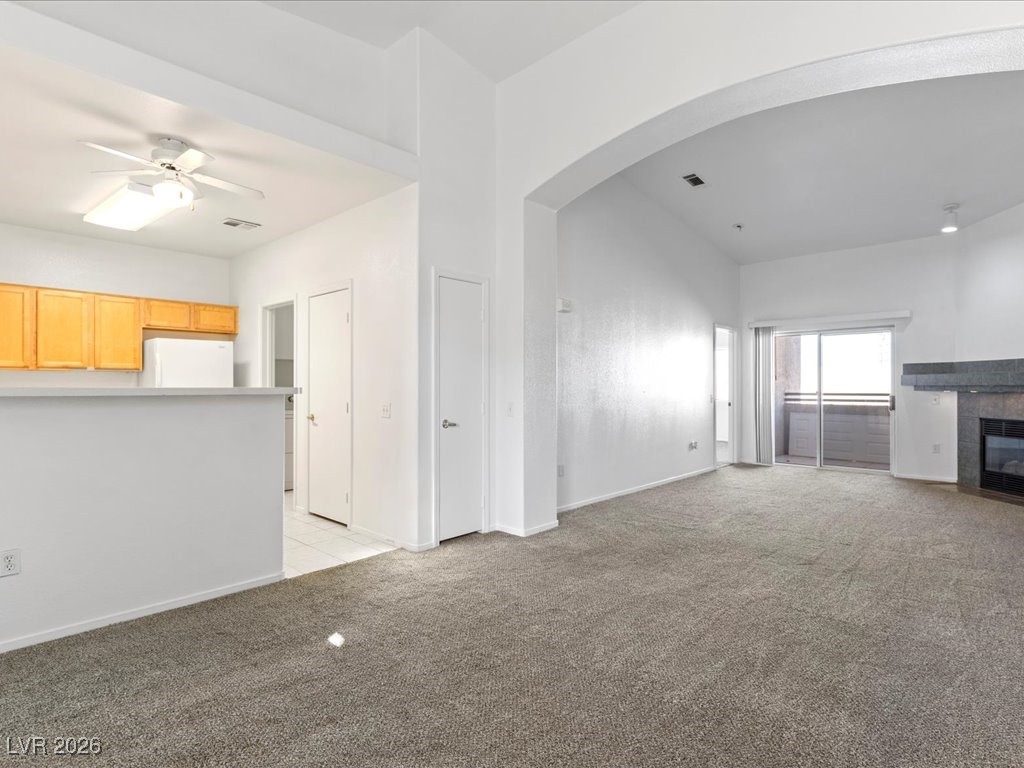8725 West Flamingo Road, Unit 235 Las Vegas, NV 89147 - Photo 5 of 22 Unfurnished living room featuring light carpet, arched walkways, a fireplace, and ceiling fan