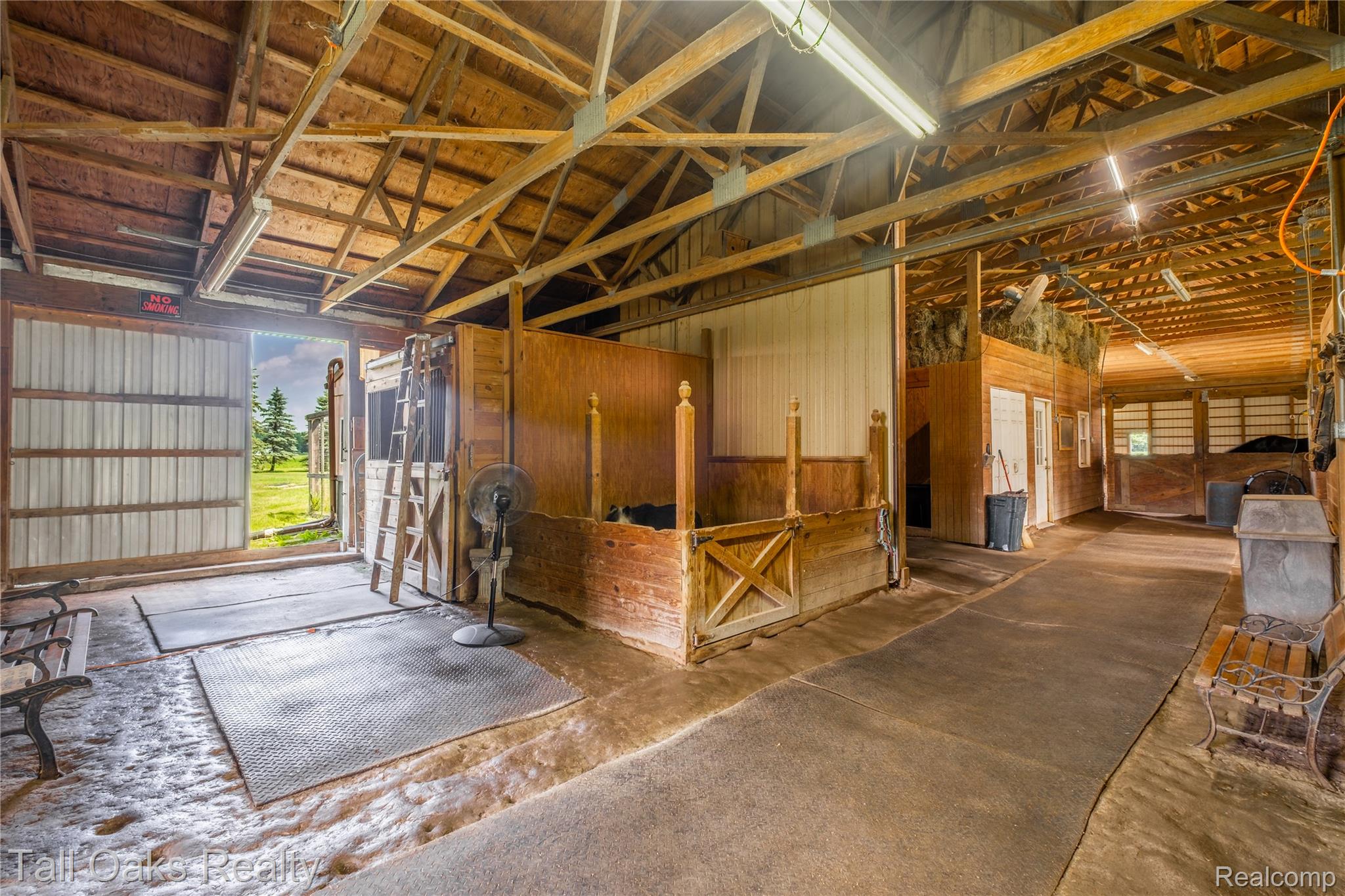 79330 Capac Road Armada, MI 48005 - Photo 13 of 42 Barn interior featuring exposed wood beam ceiling, stall enclosures with wood-finish paneling, concrete flooring, and fluorescent lighting fixtures