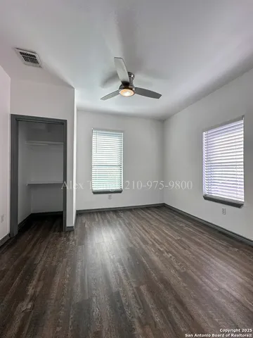 an empty room with wooden floor chandelier fan and windows