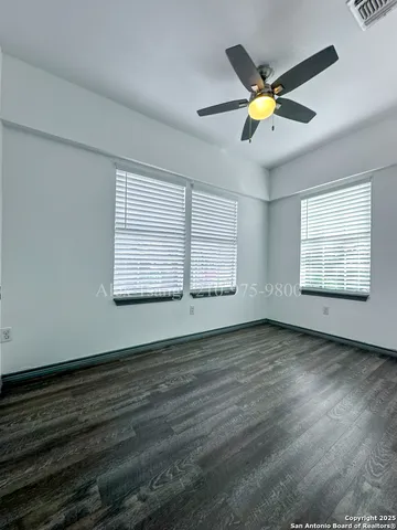 an empty room with wooden floor fan and windows