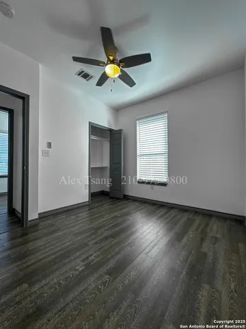 an empty room with wooden floor chandelier fan and windows