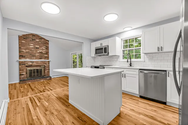 a kitchen with granite countertop a stove a sink dishwasher a refrigerator and a dining table with wooden floor