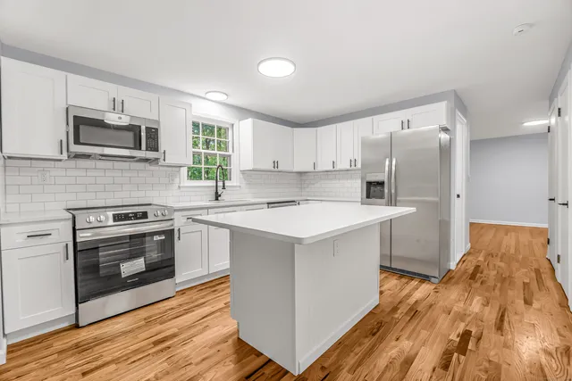 a kitchen with stainless steel appliances a stove a sink a refrigerator white cabinets and wooden floor