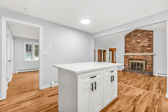 a open kitchen with granite countertop a stove top oven a sink dishwasher and white cabinets with wooden floor next to windows