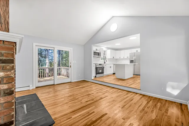 a view of empty room with wooden floor and kitchen view