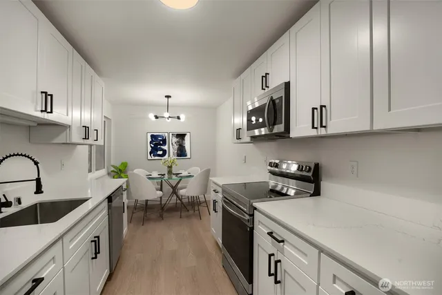 a kitchen with a sink dishwasher a stove top oven a dining table and chairs with wooden floor