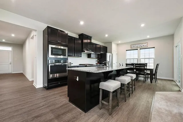 a kitchen with stainless steel appliances granite countertop a refrigerator a stove a sink a dining table and chairs with wooden floor