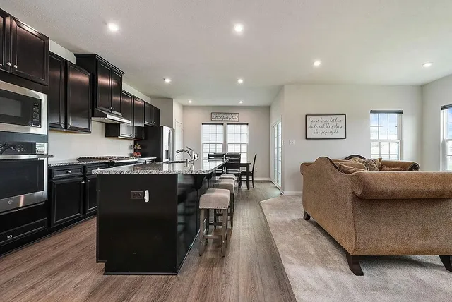 a living room with stainless steel appliances furniture and a kitchen view