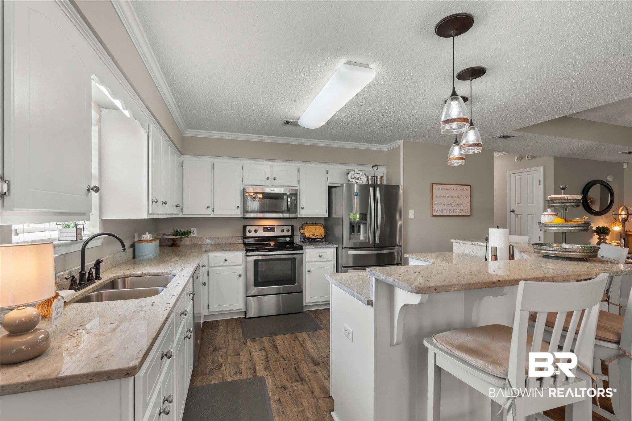 8600 Sable Court Semmes, AL 36575 - Photo 6 of 20 Kitchen with appliances with stainless steel finishes, dark wood-style flooring, white cabinetry, a breakfast bar, and a textured ceiling