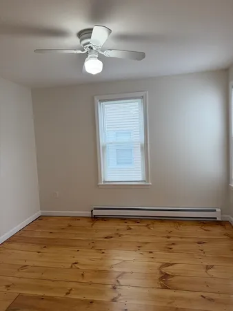 a view of an empty room with wooden floor and a ceiling fan
