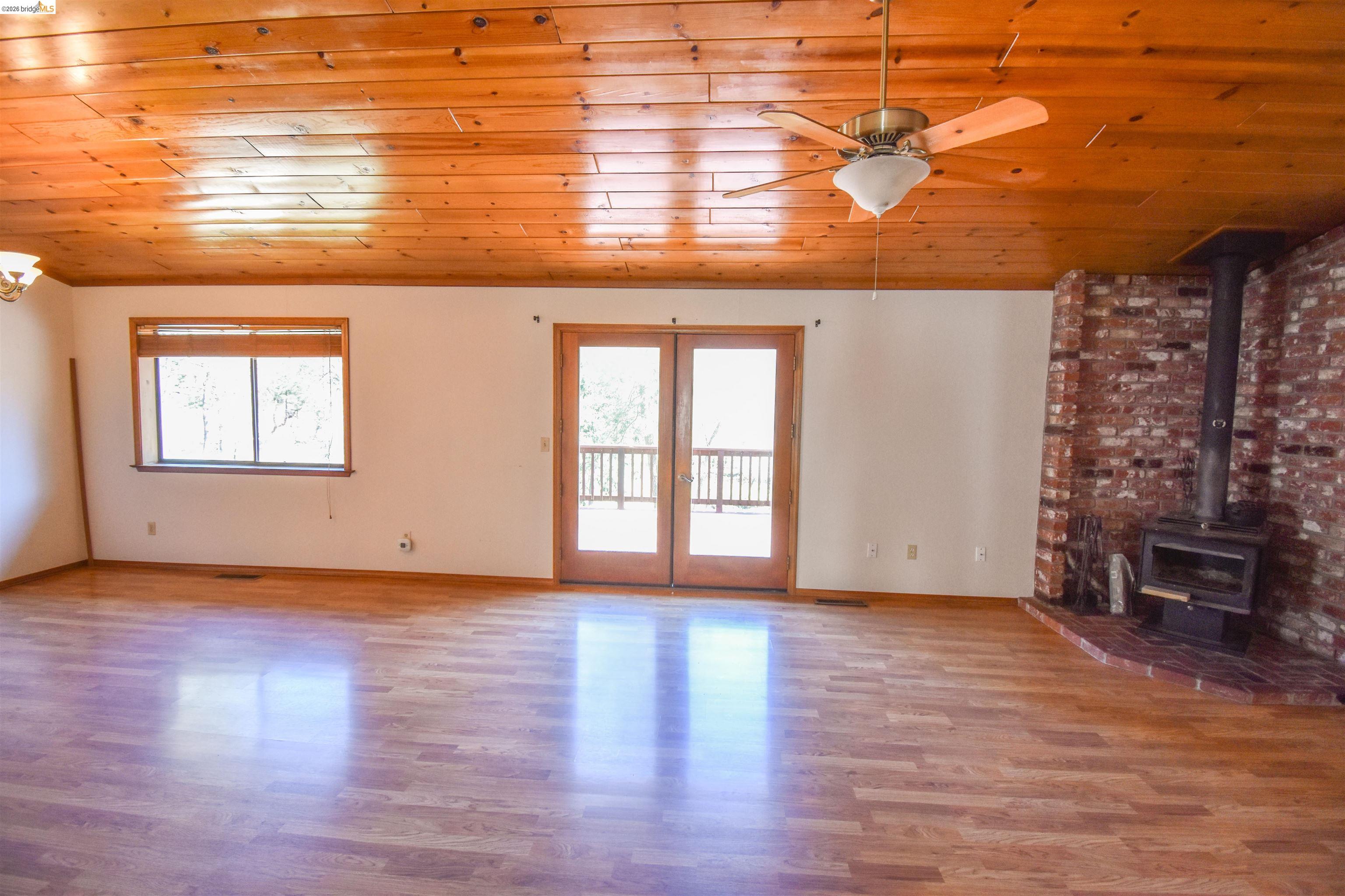 21515 Bellview Creek Road Sonora, CA 95370 - Photo 7 of 31 Unfurnished living room with wooden ceiling, a wood stove, light wood-style floors, ceiling fan, and french doors