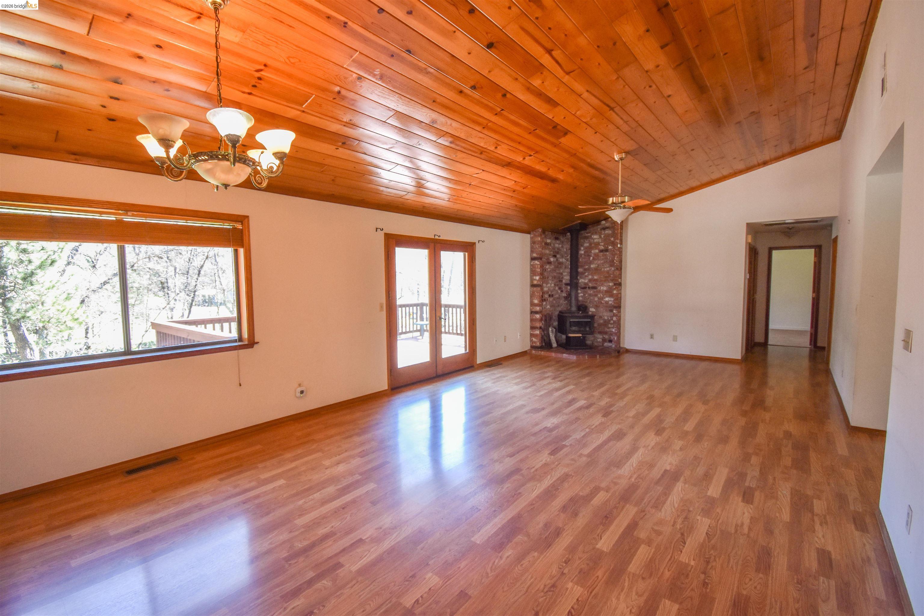 21515 Bellview Creek Road Sonora, CA 95370 - Photo 8 of 31 Unfurnished living room featuring a wood stove, a vaulted wood ceiling, light wood-style floors, a chandelier, and a ceiling fan