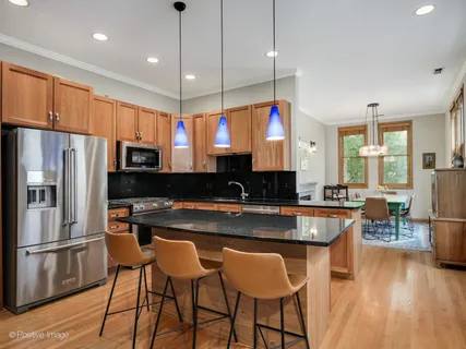 a kitchen with stainless steel appliances granite countertop a stove a refrigerator a sink a dining table and chairs with wooden floor