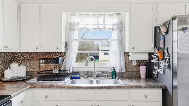 a kitchen with granite countertop a refrigerator a stove a sink and white cabinets