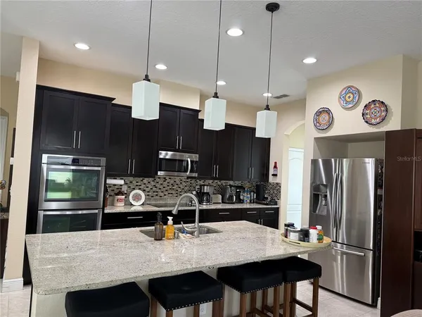 a kitchen with stainless steel appliances kitchen island granite countertop a table chairs and a refrigerator