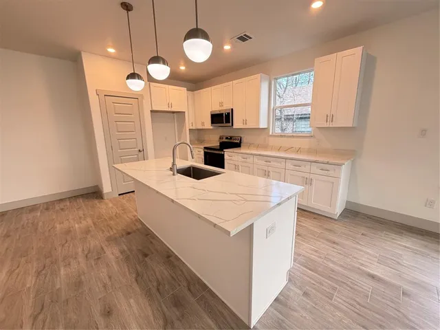 a large kitchen with stainless steel appliances a large counter top a sink a stove and a wooden floors