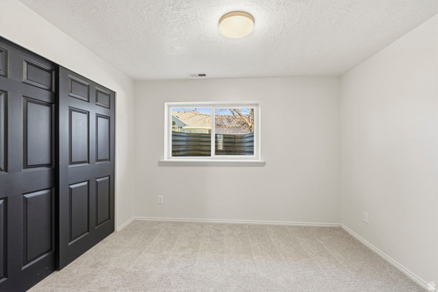 2460 Allison Way Syracuse, UT 84075 - Photo 21 of 24 Carpeted room featuring a window, built-in closet with dark paneled doors, and a ceiling-mounted light fixture