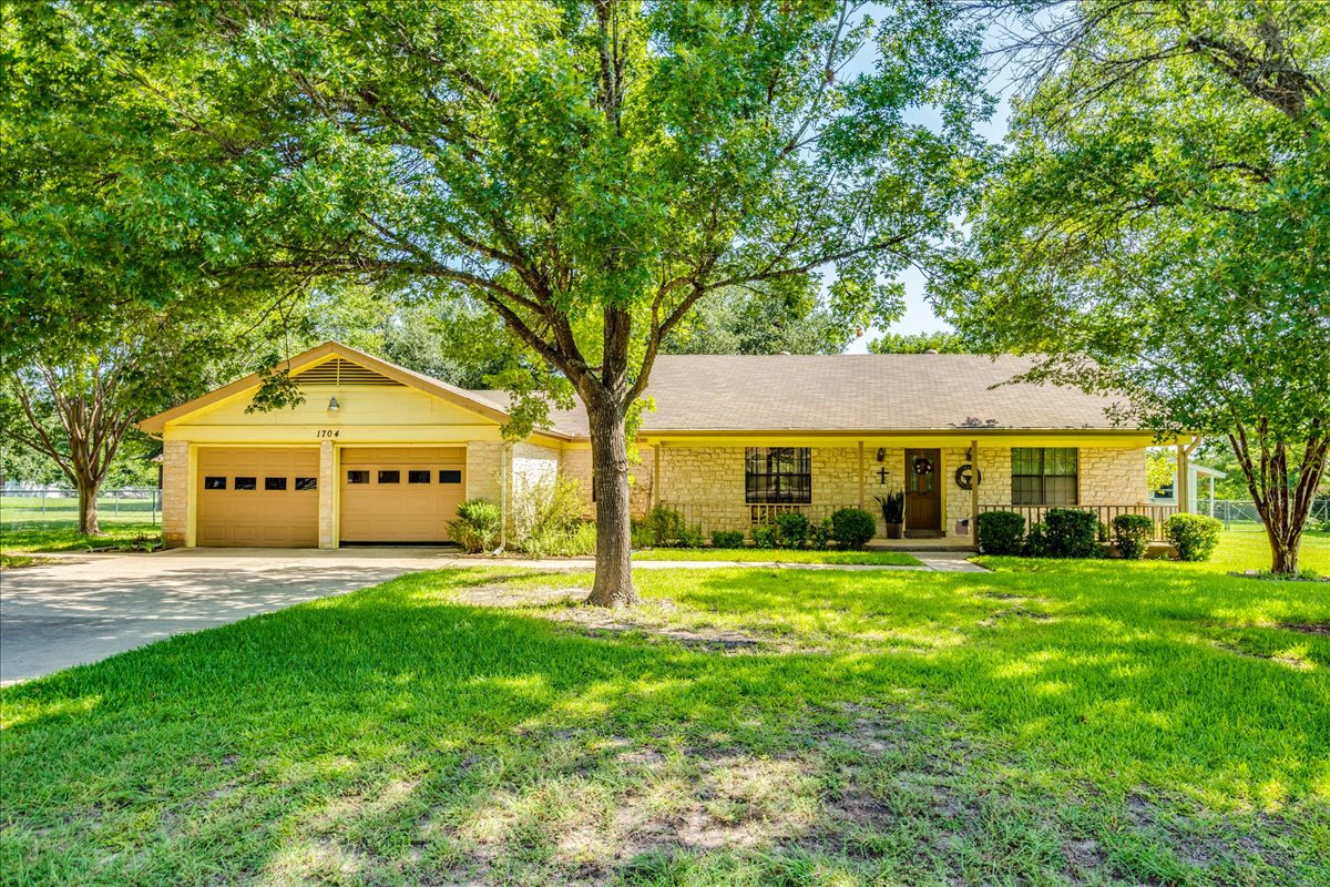 1704 Buttercup Road Pflugerville, TX 78660 - Photo 1 of 1 Mature trees shade a welcoming stone-clad ranch home with a broad driveway and covered porch.