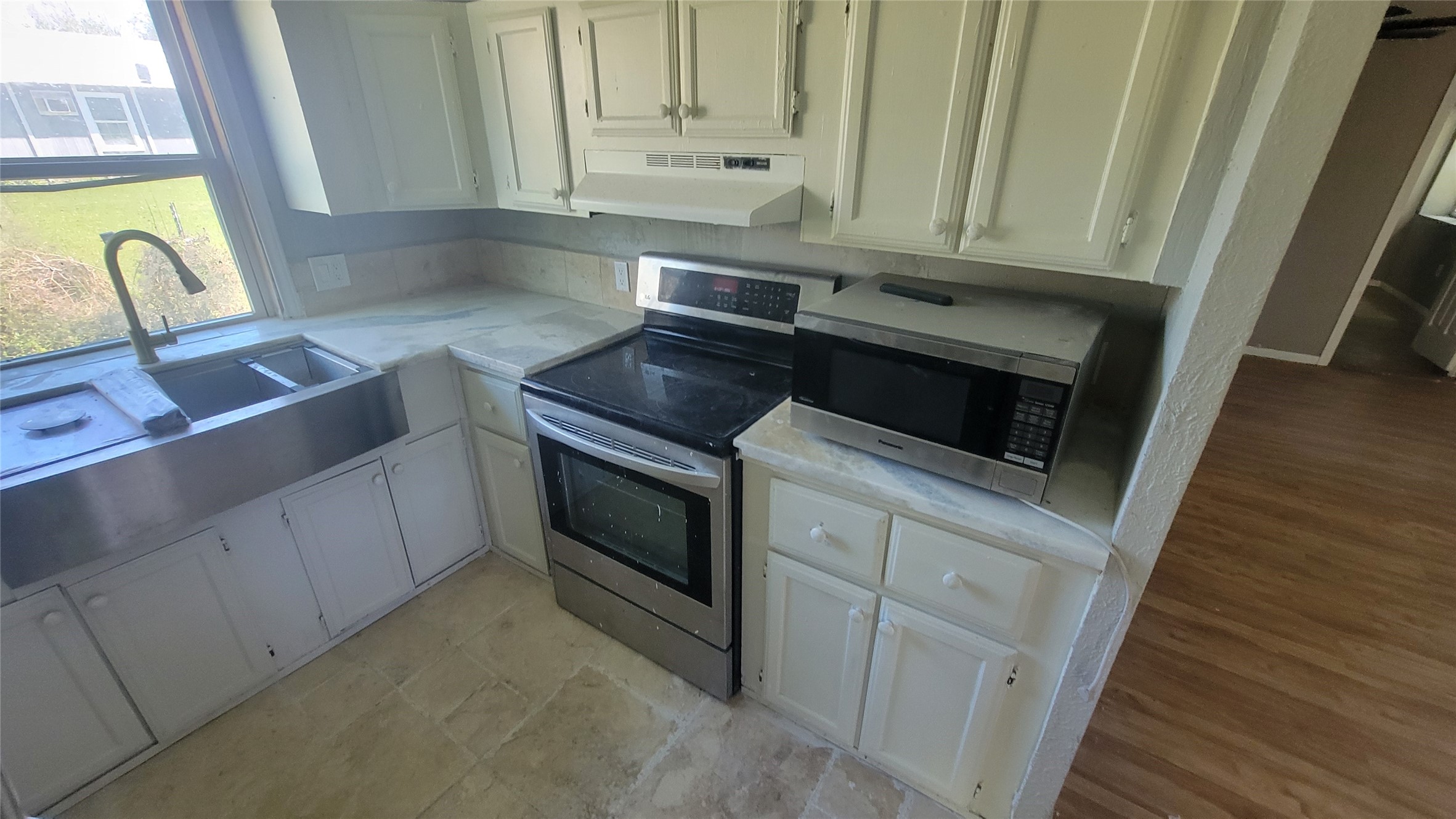 12018 Sandpiper Road Angleton, TX 77515 - Photo 36 of 48 This kitchen features white cabinetry, a stainless steel farmhouse sink, and a modern electric stove with a microwave. The space is brightened by a large window and has a tiled floor with adjacent wood flooring.
