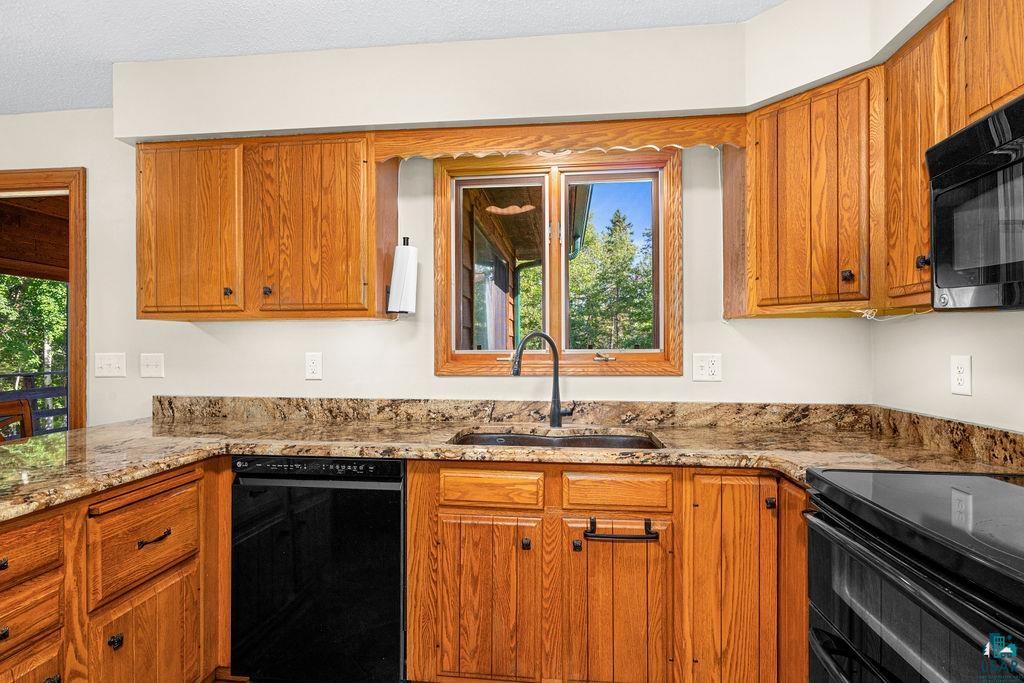 5370 Ugstad Road Hermantown, MN 55811 - Photo 42 of 68 Wood cabinetry, stone countertops, black undermount sink, black faucet, and black appliances