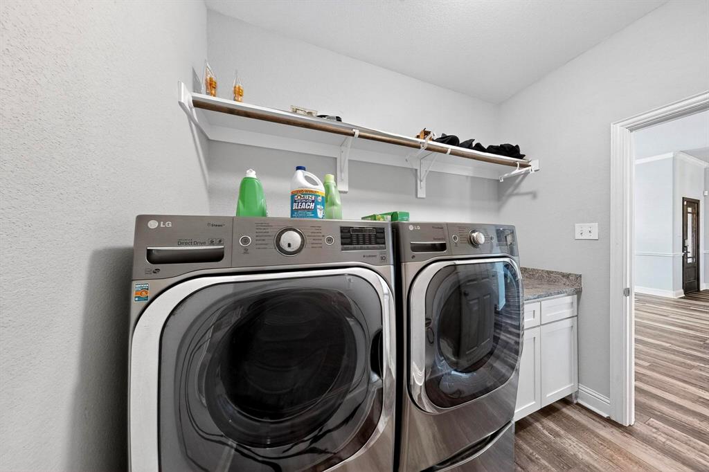 634 Gant Road Sherman, TX 75090 - Photo 27 of 40 Dedicated laundry space featuring a side-by-side washer and dryer, upper shelving, white cabinetry with a stone-finish countertop, and wood-finish flooring