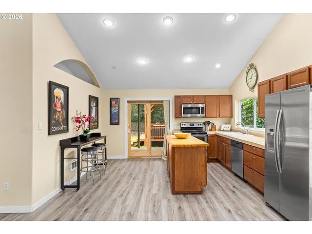 a living room with stainless steel appliances furniture wooden floor and a kitchen view