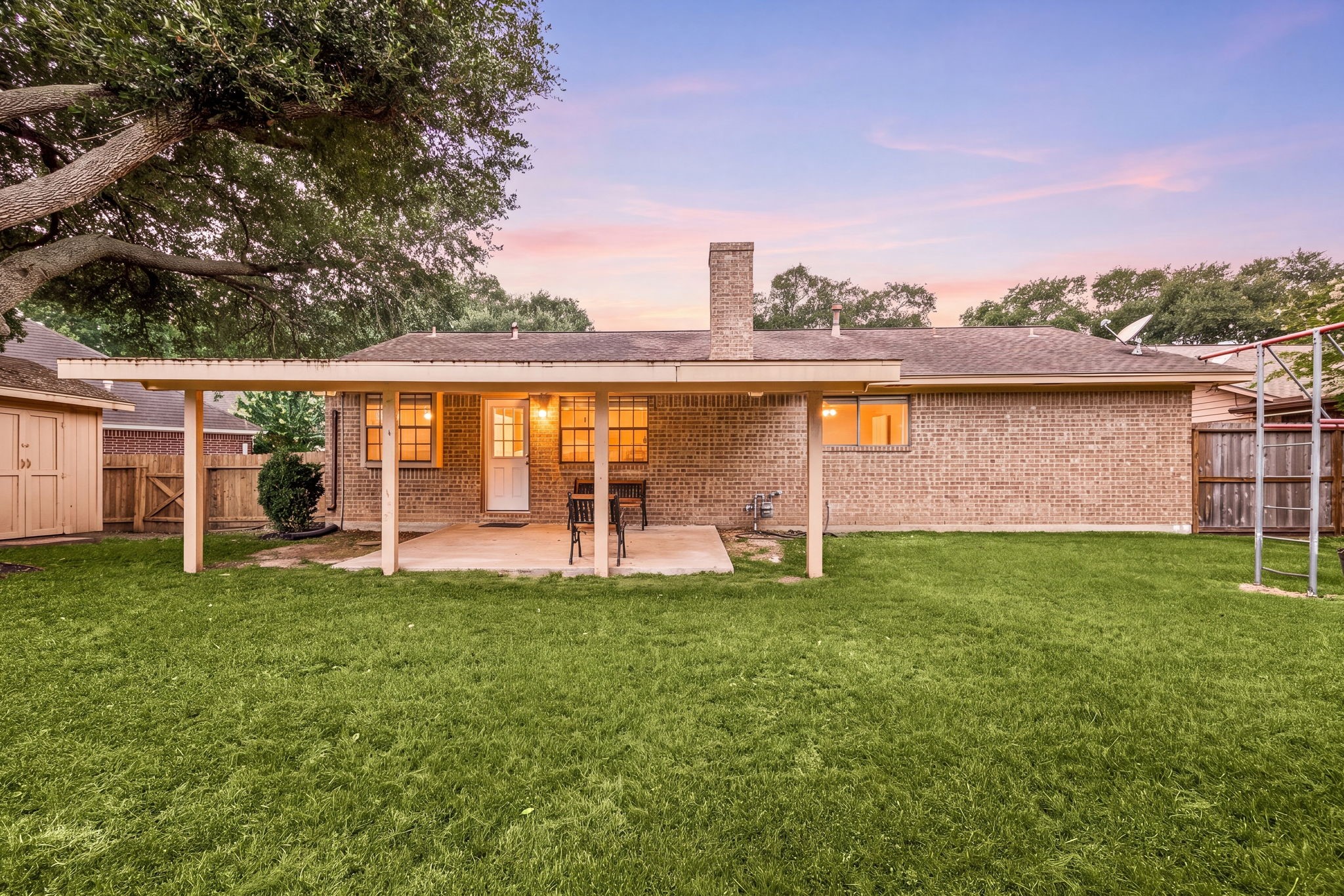 2019 Franklin Circle Rosenberg, TX 77471 - Photo 15 of 19 As evening settles in, the large fenced backyard glows beneath mature shade trees, with a full-length covered patio extending the living space outdoors.