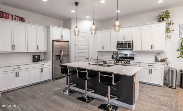 a kitchen with stainless steel appliances kitchen island granite countertop a refrigerator a stove a sink a dining table and chairs with wooden floor