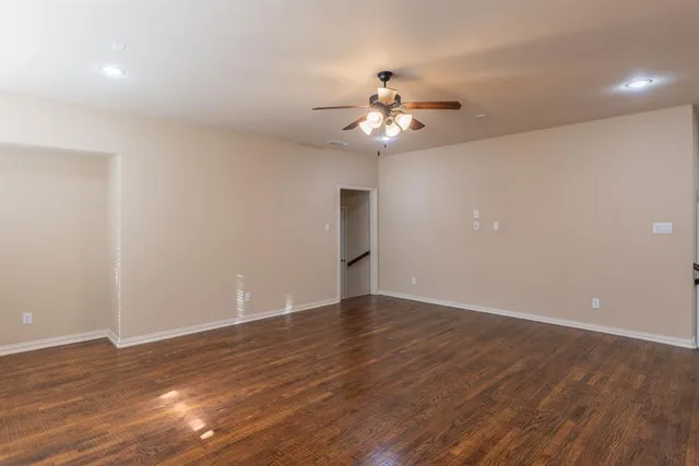 a view of an empty room with wooden floor and a ceiling fan