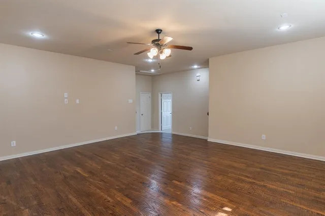 an empty room with wooden floor fan and windows