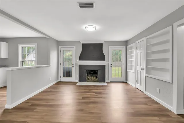 an empty room with wooden floor fireplace and windows