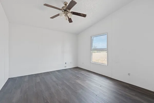 an empty room with wooden floor ceiling fan and windows
