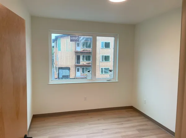 a view of an empty room with wooden floor and a window