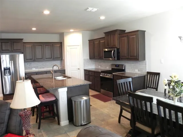 a kitchen with stainless steel appliances granite countertop a table chairs microwave and refrigerator