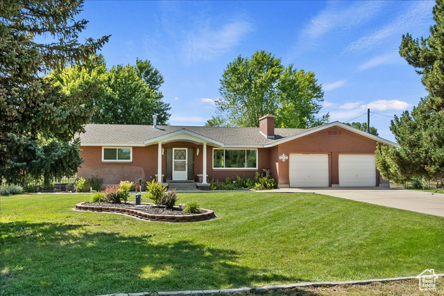 Ranch-style home featuring an attached garage, a chimney, concrete driveway, and a front lawn