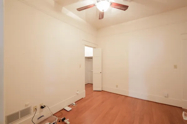 an empty room with a chandelier fan and wooden floor