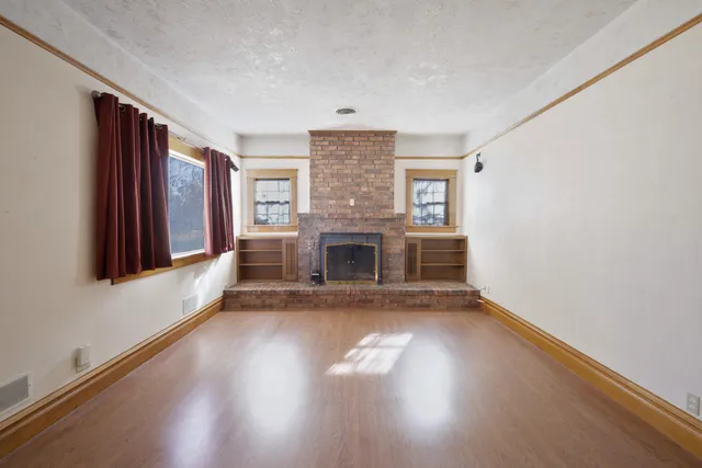 an empty room with wooden floor fireplace and windows