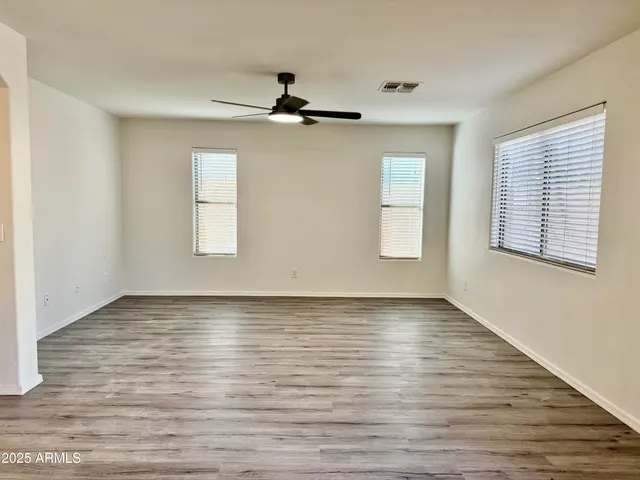 an empty room with wooden floor fan and windows