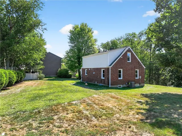 a house that is sitting in the grass with large trees and plants
