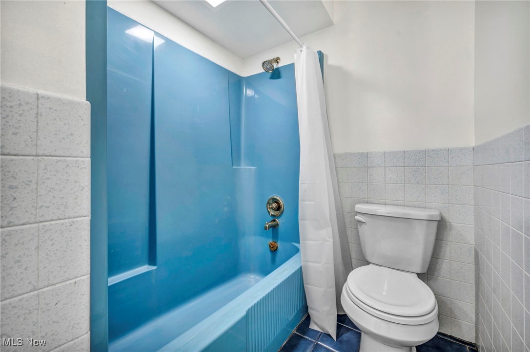 38814 Johnnycake Ridge Road Willoughby, OH 44094 - Photo 26 of 48 Full bathroom with shower / tub combo with curtain, toilet, tile patterned flooring, tile walls, and wainscoting