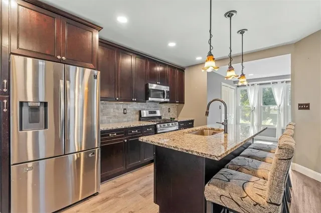 a kitchen with stainless steel appliances granite countertop a refrigerator a sink dishwasher a stove and a refrigerator with wooden floor