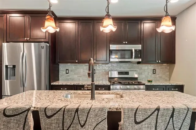 a kitchen with stainless steel appliances kitchen island granite countertop a refrigerator a stove a microwave oven a sink with island and chairs