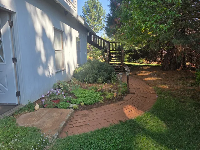 a view of a barn with big yard plants and large trees