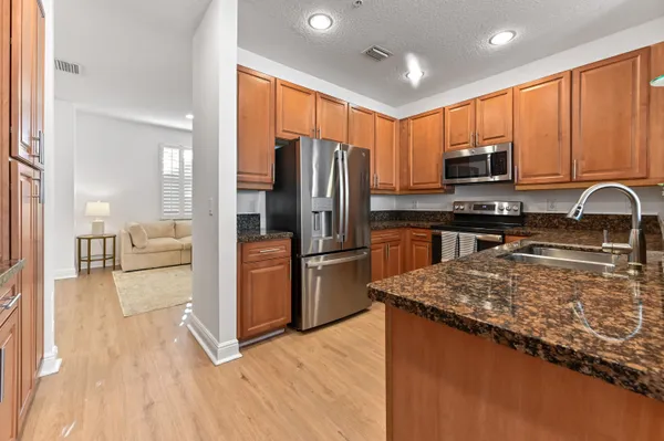 a kitchen with stainless steel appliances granite countertop a refrigerator a sink dishwasher a stove and a oven with wooden floor