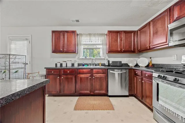 a kitchen with stainless steel appliances granite countertop a stove a sink dishwasher and a microwave oven with wooden cabinets