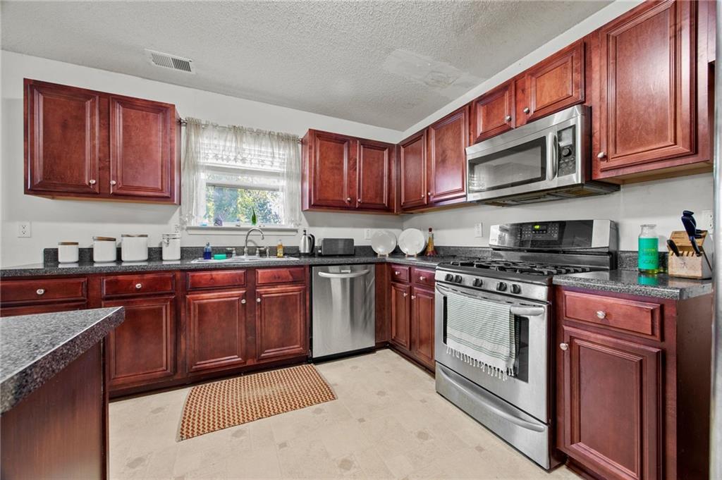 407 Grier Drive Locust Grove, GA 30248 - Photo 13 of 38 a kitchen with stainless steel appliances granite countertop a stove a sink dishwasher and a microwave oven with wooden cabinets