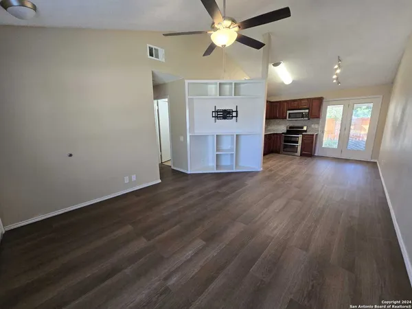 an empty room with wooden floor ceiling fan and windows