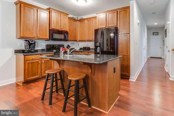 a kitchen with stainless steel appliances granite countertop wooden cabinets a refrigerator a stove a sink and dishwasher with wooden floor